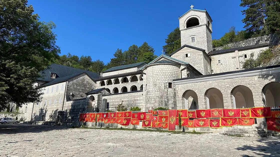 The stone buildings and bell tower of Cetinje Monastery hung with Montenegrin flags, in the old royal capital